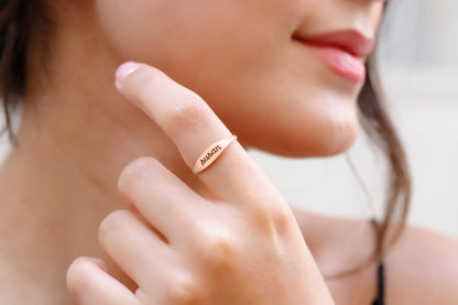A close-up image of a woman's finger wearing a rose gold-filled stackable ring with an engraved name.