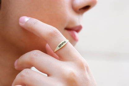 A close-up image of a woman's finger wearing a gold-filled stackable ring with an engraved name.
