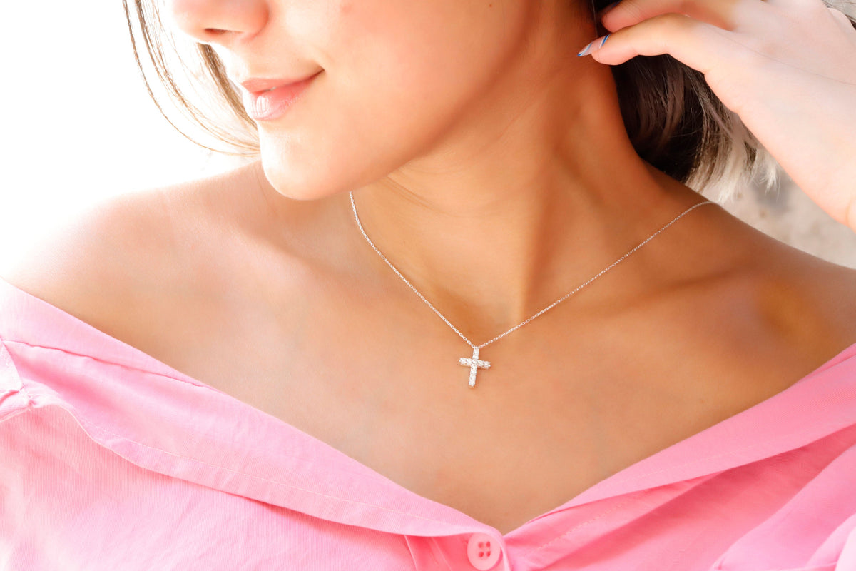 A close-up image of a woman wearing a 925 sterling silver, diamond cross necklace with a pendant cross on her neck.