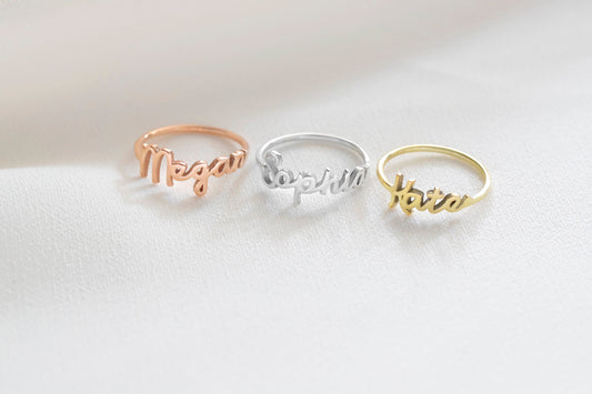 A close-up image of 3 rings with the name 'Sophia' 'Megan' 'Kate' written on it, worn on a person's finger in gold silver and rose finishes.