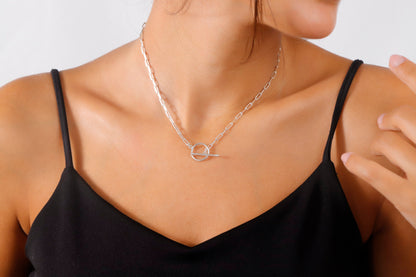 A close-up image of a woman wearing a black tank top showcasing an 18k gold link chain necklace with a paperclip design and a sailor clasp.