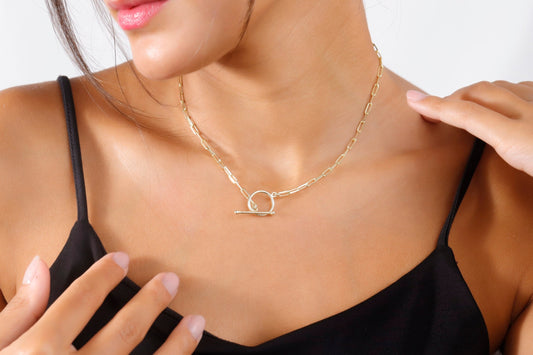 A close-up image of a woman wearing a black tank top showcasing an 18k gold link chain necklace with a paperclip design and a sailor clasp.