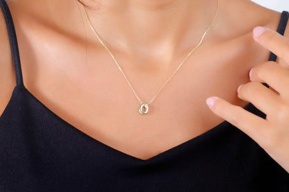 A close-up image of a woman wearing a gold-filled balloon necklace with a single letter '0' pendant.