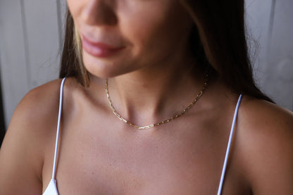 A close-up image of a person wearing a gold-filled loop chain necklace with a delicate and dainty design.