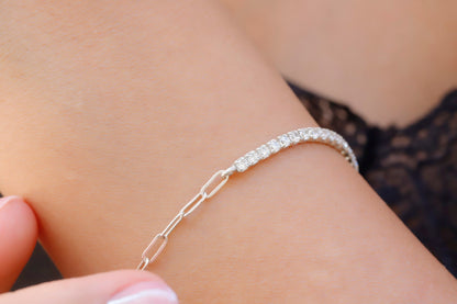 A close-up image of a tennis bracelet combined with a paperclip chain, displayed on a person's wrist.