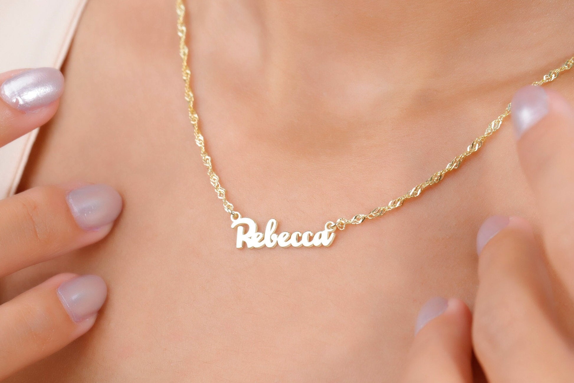 Gold necklace with 'Rebecca' pendant on a person's neck