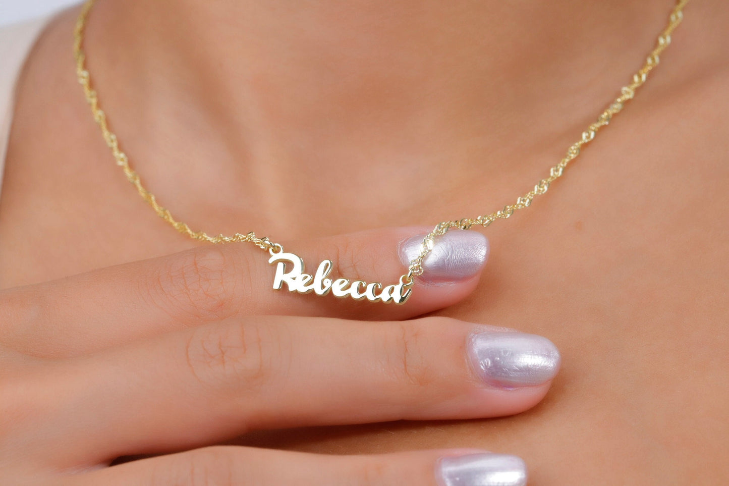 Gold necklace with 'Rebecca' pendant on a hand