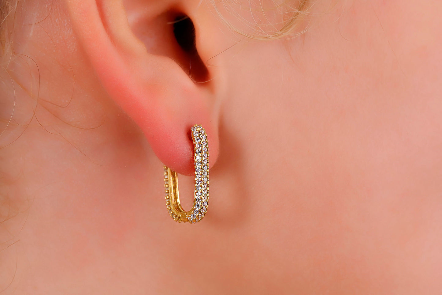 Close-up of a person wearing gold hoop earrings with clear stones.