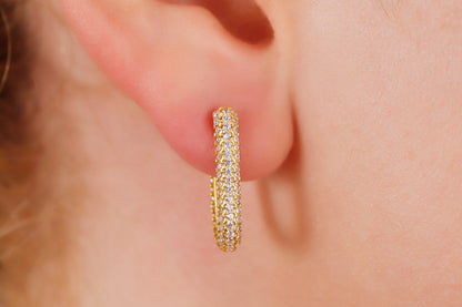 Gold hoop earring worn on an ear with a blurred background