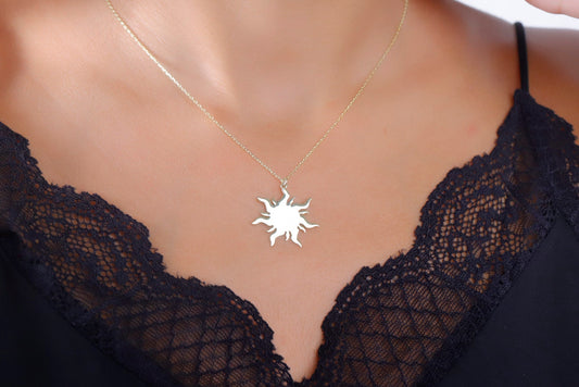 A woman wearing a dainty 14K gold sun necklace with a delicate chain, displayed against a lace neckline.