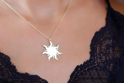 A woman wearing a dainty 14K gold sun necklace with a delicate chain, displayed against a lace neckline.