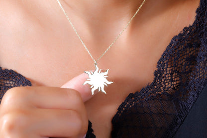 A woman wearing a dainty 14K gold sun necklace with a delicate chain, displayed against a lace neckline.