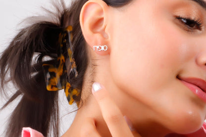 A close-up image of a woman's ear wearing a small gold-colored stud earring with a personalized Hebrew name.