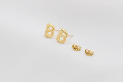 A close-up image of a gold initial stud earring, on a white background.
