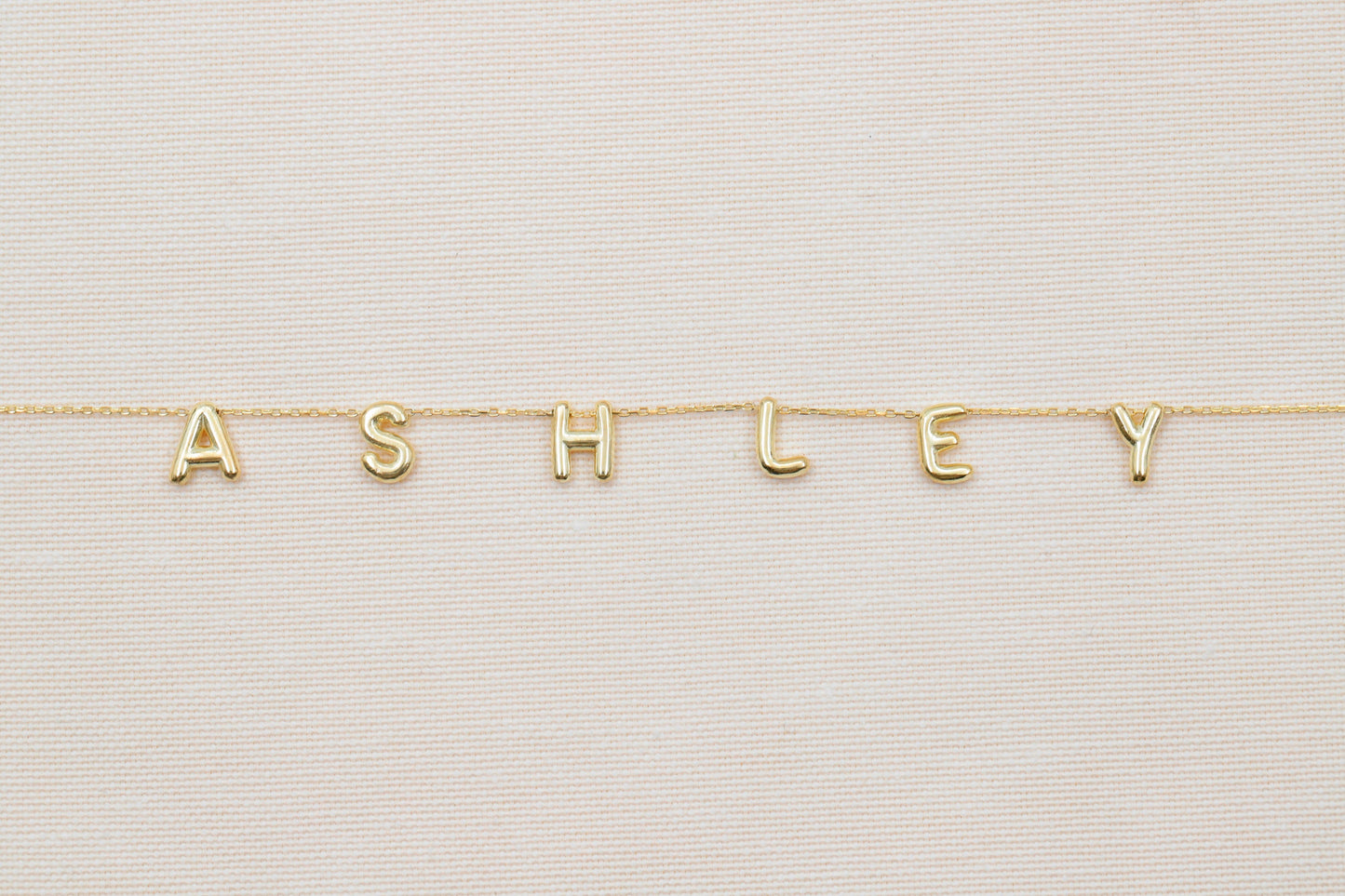 Gold necklace with 'ASHLEY' letters on a light background