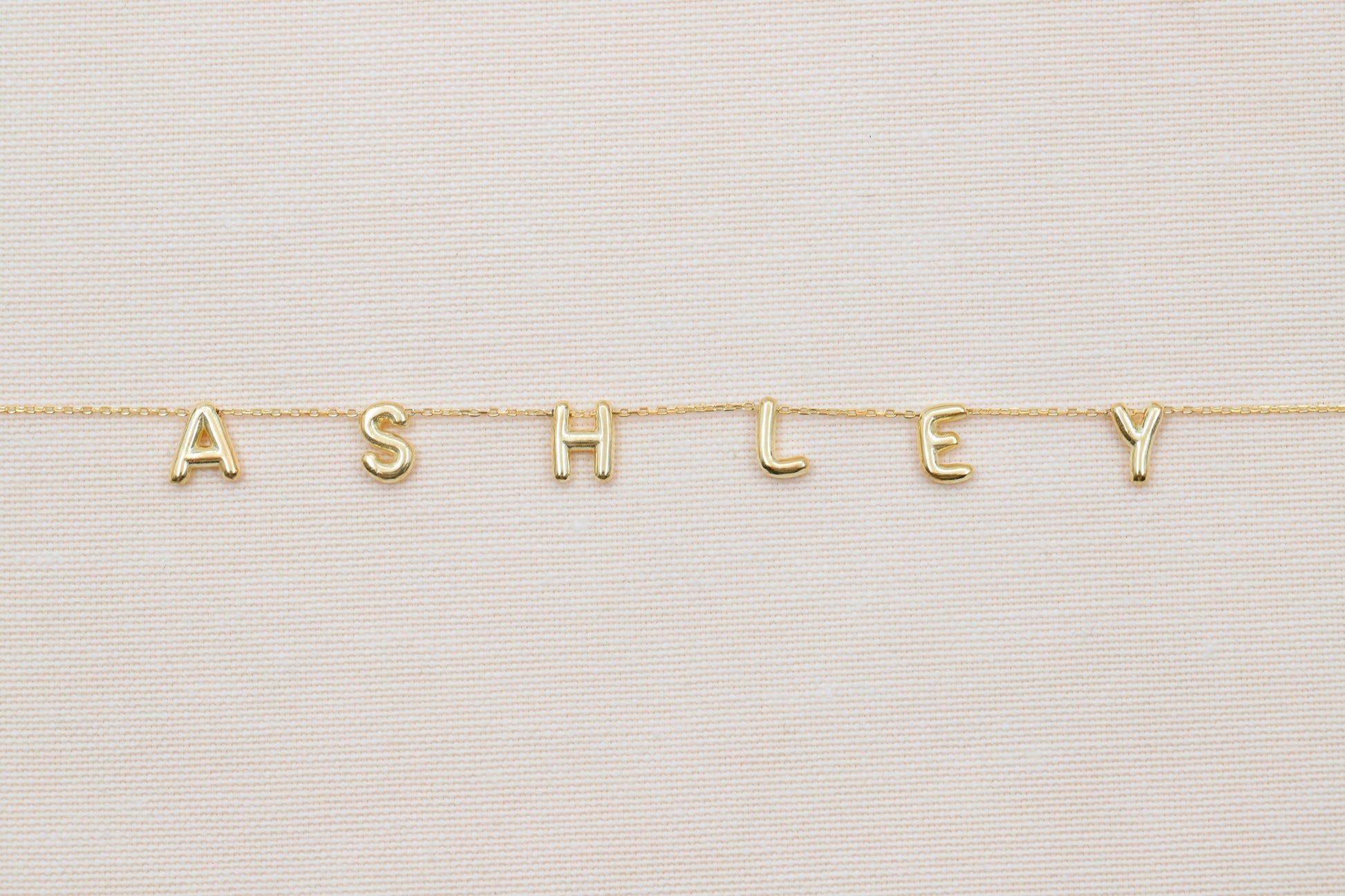 Gold necklace with 'ASHLEY' letters on a light background