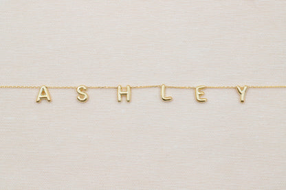 Gold necklace with 'ASHLEY' letters on a light background