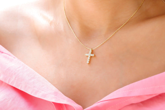 A close-up image of a woman wearing a gold-filled, diamond cross necklace with a pendant cross on her neck.