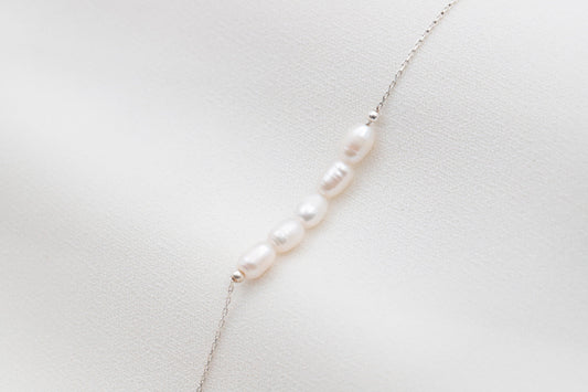 a white pearl beaded bracelet with gold accents on white background.