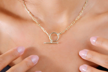 A close-up image of a woman wearing a black tank top showcasing an 18k gold link chain necklace with a paperclip design and a sailor clasp.