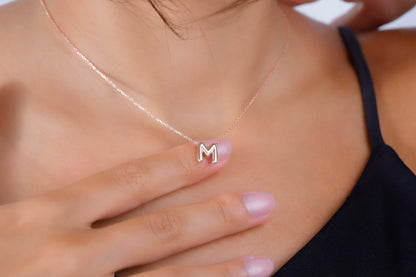 A close-up image of a woman wearing a gold-filled balloon necklace with a single letter 'M' pendant.