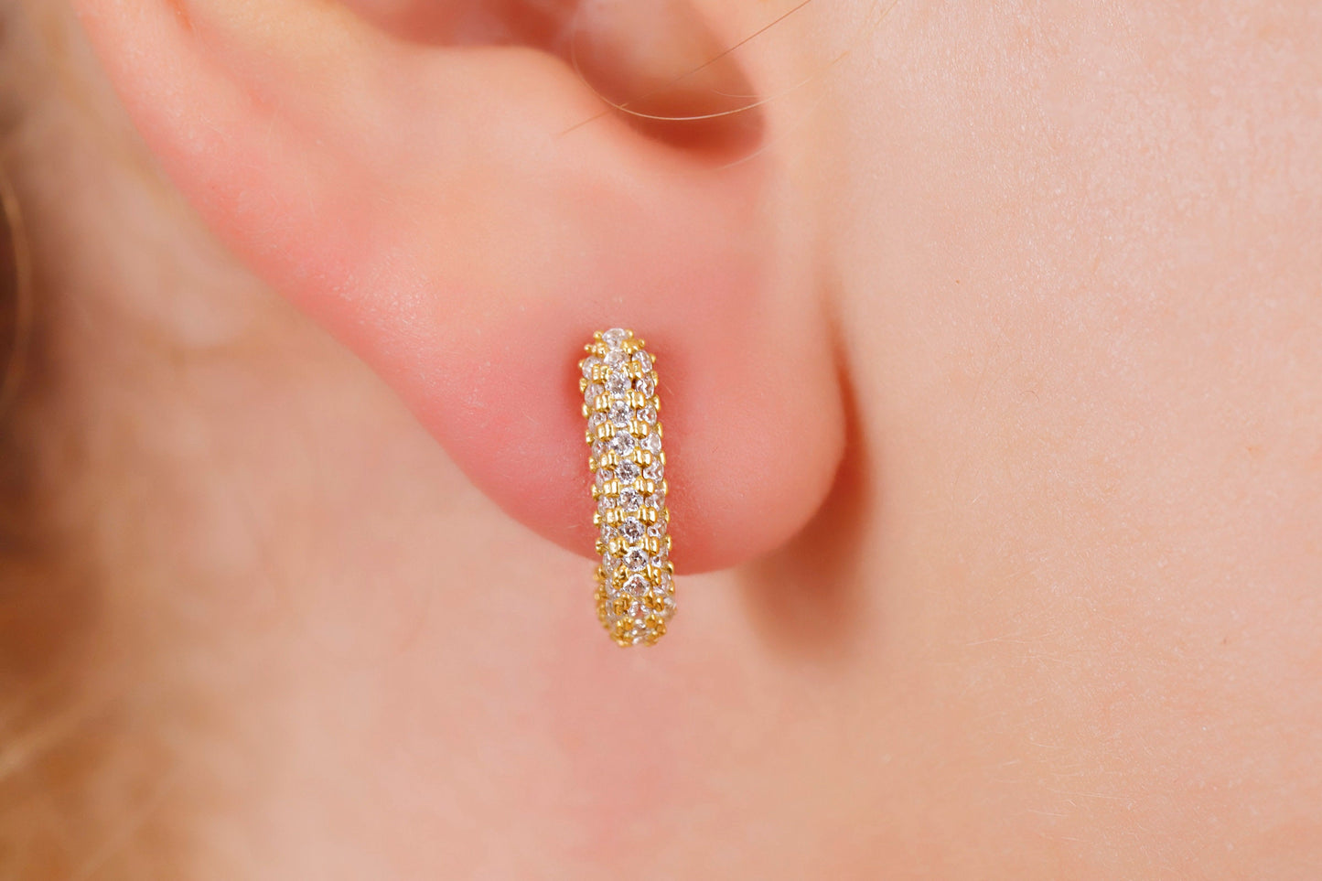 Gold hoop earring worn on a person's ear with a soft focus background
