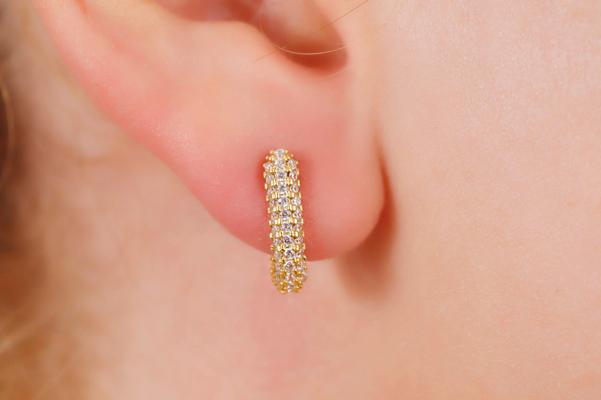 Gold hoop earring worn on a person's ear with a soft focus background