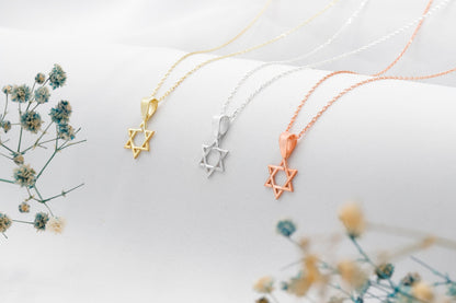 Three star-shaped pendants on gold, silver, and rose gold necklaces with a blurred floral background.