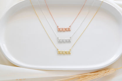 A close-up image of a woman wearing a silver-colored necklace with a 3D balloon-shaped pendant that reads 'mama'.