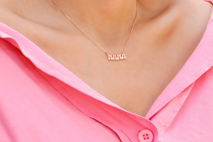 A close-up image of a woman wearing a rose-colored necklace with a 3D balloon-shaped pendant that reads 'mama'.