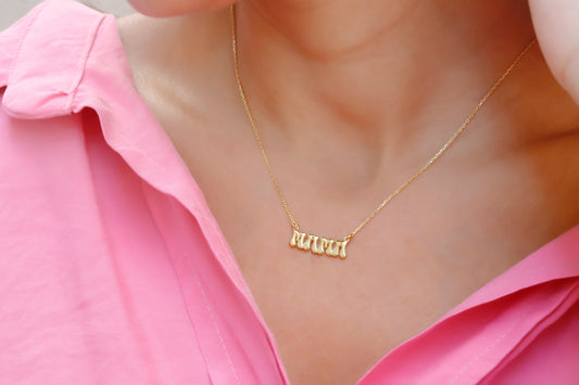 A close-up image of a woman wearing a goldcolored necklace with a 3D balloon-shaped pendant that reads 'mama'.