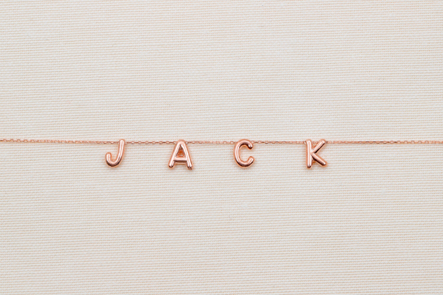 Rose gold 'JACK' necklace on a textured beige background