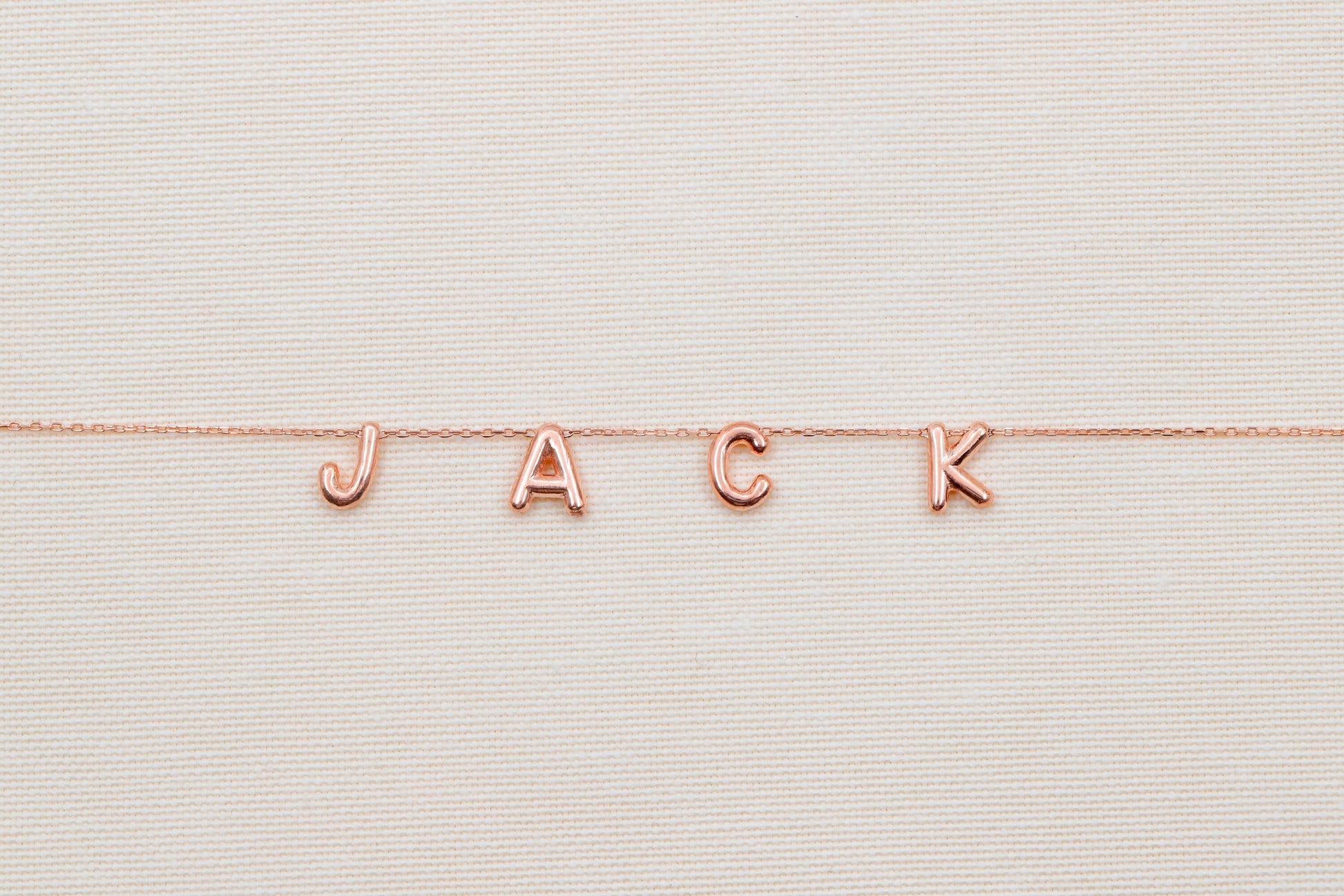Rose gold 'JACK' necklace on a textured beige background