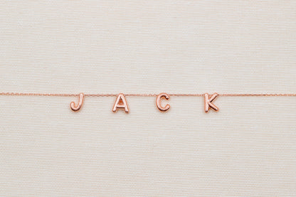 Rose gold 'JACK' necklace on a textured beige background
