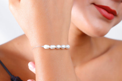A woman wearing a white pearl beaded bracelet with gold accents on her wrist.