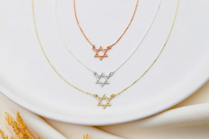 A close-up image of a gold rose gold and silver Star of David necklace.