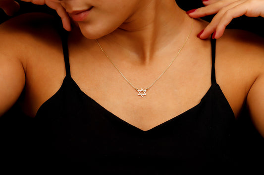 A close-up image of a person wearing a black tank top showcasing a gold Star of David necklace.