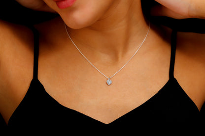 A close-up image of a woman wearing a silver pave diamond heart necklace with a silver chain, showcased on a black dress.