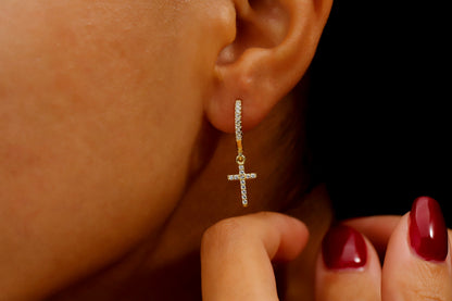 A close-up image of a woman's ear wearing a gold-filled diamond cross dangle earring.