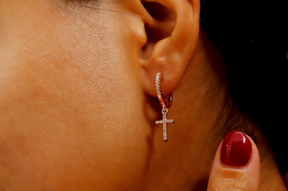 A close-up image of a woman's ear wearing a rose gold-filled diamond cross dangle earring.