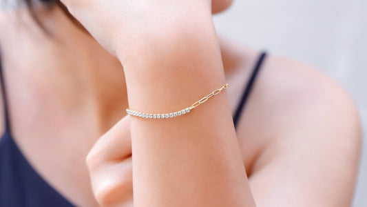 A close-up image of a person's wrist wearing a gold-colored half tennis half link chain bracelet with dainty CZ white diamonds.