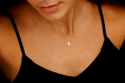 A close-up image of a woman wearing a gold initial necklace with the letter 'E' on a delicate chain. a product by SilverGoldandRose.com .