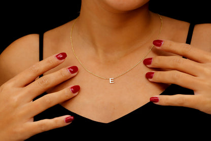 A person wearing a thin gold filled over 925 sterling silver necklace with a small, minimalist "E" initial charm. A product by SilverGoldandRose.com.