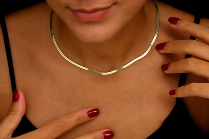 Gold necklace worn by a person with red nail polish on their fingers.