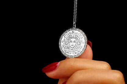 A close-up image of a person's fingers holding a silver necklace with a circular pendant featuring a design.