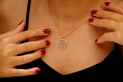 Necklace with a circular pendant worn by a person with red nail polish.