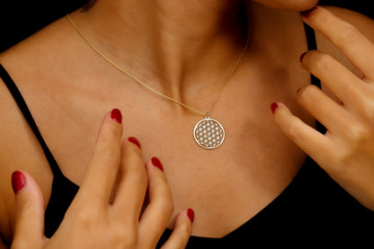 Necklace with a circular pendant worn by a person with red nail polish on their fingers.