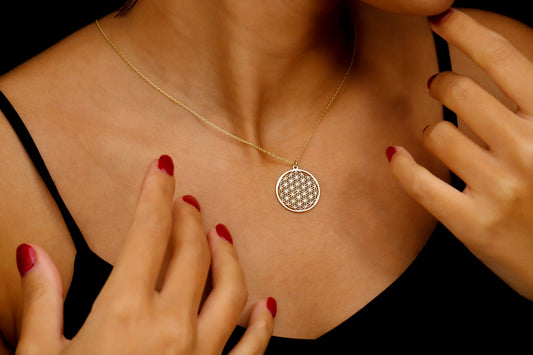 A close-up image of a person wearing a gold-filled pendant necklace with the Flower of Life design.