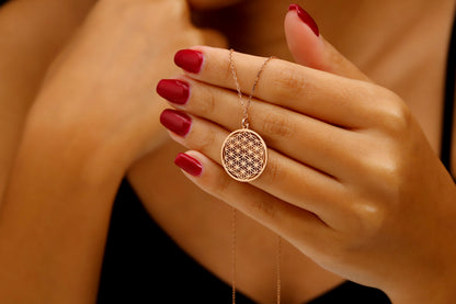 Rose gold necklace with floral design pendant held by a hand with red nail polish.