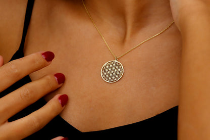 Gold necklace with a circular pendant worn by a person with red nail polish.